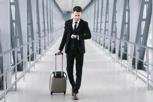Boarding Time. Confident man checking time on watch, walking with suitcase in airport, going to departure gate photo