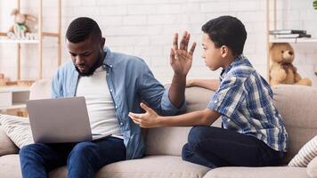 Little Afro Son Asking Attention From His Father Busy With Laptop, Working Man Ignoring His Kid And Showing Stop Gesture With Hand photo