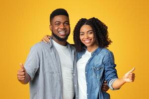 Great choice. Happy african american couple gesturing thumbs up, recommending something, posing together on yellow background with copy space photo