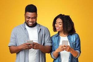 Curious black girlfriend peeking into boyfriend's smartphone, trying to read his messages, yellow studio background with copy space photo