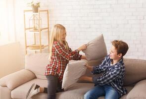 Happy Brother And Sister Having Pillow Fight Laughing And Playing Together On Couch At Home. Siblings Friendship photo