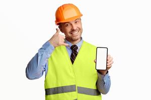Call Me. Builder Workman Showing Cellphone Blank Screen Gesturing Recommending Building And Repair Services Over White Studio Background. Mockup photo