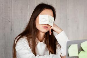 A lot of work concept. Tired freelancer sleeping at workplace with stickers on eyes photo