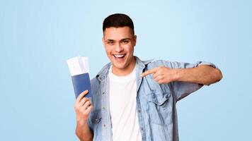 Traveling abroad. Emotional young man pointing at passport with tickets over orange background, panorama photo