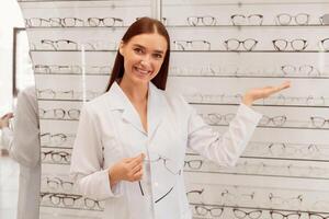 Beautiful lady ophthalmologist seller showing range of eyeglasses frame in optical store photo