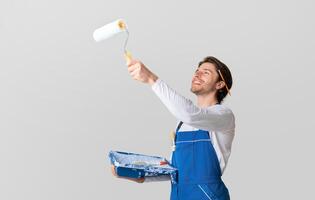 Happy painter dressed in work clothes painting ceiling with roller, low angle view, copy space photo