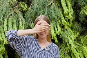 Woman wearing elegant clothes hiding her face standing in the forest against fir trees. photo