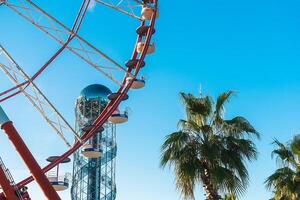 View of the Ferris wheel and the Alphabet Tower against a background of blue sky between palm trees. Ferris wheel and Alphabet Tower in the Georgian city of Batumi. photo