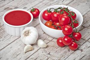 Fresh tomatoes in white bowl, sauce and raw garlic on rustic wooden table. photo