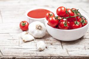 Fresh tomatoes in white bowl, sauce and raw garlic on rustic wooden table. photo