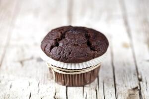 Fresh single chocolate dark muffin on rustic wooden table. photo