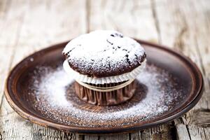 Dark chocolate muffin with sugar powder on brown plate. photo