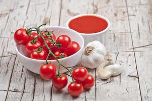 Fresh tomatoes in white bowl, sauce and raw garlic on rustic wooden table. photo