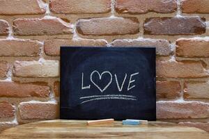 Black board with the word Love drown by hand on wooden table on brick wall background. photo