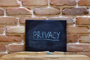 Black board with the word Privacy drown by hand on wooden table on brick wall background. photo