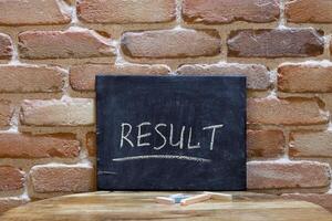 Chalk board with the word RESULT drown by hand on wooden table on brick wall background. photo