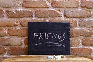 Black board with the word FRIENDS drown by hand on wooden table on brick wall background. photo