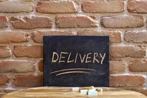 Chalk board with the word DELIVERY drown by hand on wooden table on brick wall background. photo
