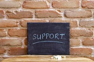 Black board with the word SUPPORT drown by hand on wooden table on brick wall background. photo
