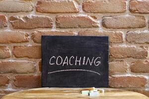 Chalk board with the word COACHING drown by hand on wooden table on brick wall background. photo