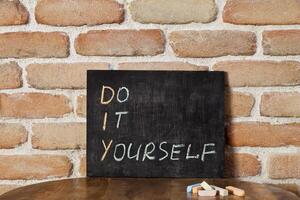 Black chalkboard with the phrase DO IT YOURSELF drown by hand on wooden table on brick wall background. photo
