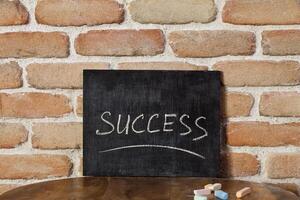 Chalk board with the word SUCCESS drown by hand on wooden table on brick wall background. photo