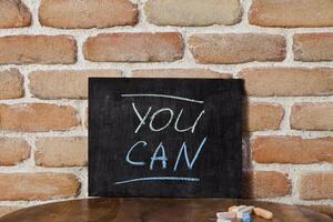Black board with the phrase YOU CAN drown by hand on wooden table on brick wall background. photo