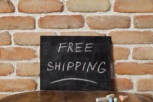 Black chalkboard with the phrase FREE SHIPPING drown by hand on wooden table on brick wall background. photo