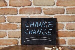 Black board with the phrase CHANCE CHANGE drown by hand on wooden table on brick wall background. photo