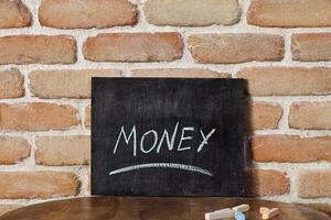 Chalk board with the word MONEY drown by hand on wooden table on brick wall background. photo