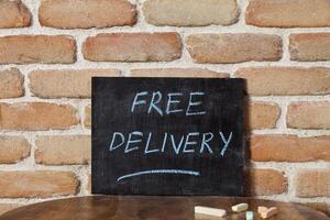 Black chalkboard with the phrase FREE DELIVERY drown by hand on wooden table on brick wall background. photo
