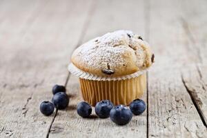 Fresh baked homemade muffin with sugar power and blueberries on rustic wooden table. photo