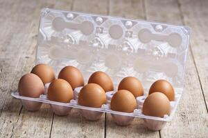 Fresh chicken eggs on plastic container on rustic wooden table. photo