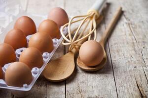 Fresh chicken eggs on plastic container and kitchen utensil on rustic wooden table background. photo
