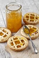 Fresh baked tarts with marmalade filling and apricot jam in glass jar on cutting board on rustic wooden table. photo