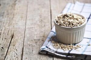 Oat flakes in ceramic bowl on linen napkin, golden wheat ears on rustic wooden background. photo