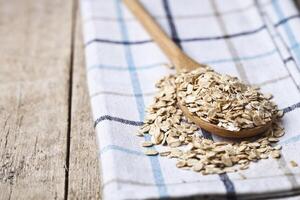Oat flakes in wooden spoon on linen napkin, golden wheat ears on rustic wooden background. photo