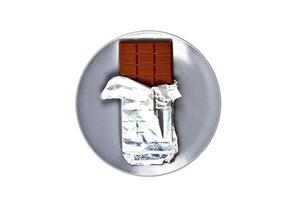 Chocolate bar with foil on grey ceramic plate isolated on white background. photo