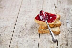 Toasted cereal bread slices stack with homemade cherry jam and spoon closeup on rustic wooden table background. photo