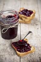 Toasted cereal bread slices and jar with homemade wild berries jam and spoon closeup on rustic wooden table background. photo