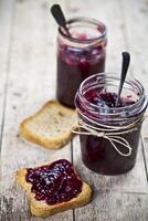 Toasted cereal bread slices and jars with homemade wild berries and cherry jam and spoons closeup on rustic wooden table background photo