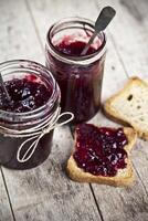Toasted cereal bread slices and jars with homemade wild berries and cherry jam and spoons closeup on rustic wooden table background photo