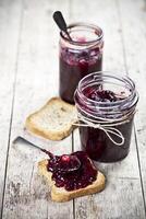 Cereal fresh bread toasts slices and jars with homemade wild berries and cherry jam and spoons closeup on rustic wooden table background. photo