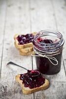 Toasted cereal bread slices and jar with homemade wild berries jam and spoon closeup on rustic wooden table background. photo