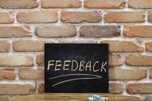 Chalk board with the word FEEDBACK drown by hand and chalks on wooden table on brick wall background. photo