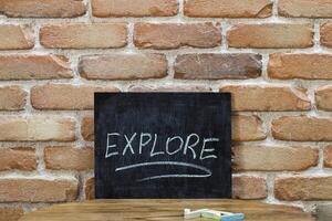 Chalk board with the word EXPLORE drown by hand and chalks on wooden table on brick wall background. photo