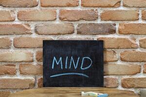 Chalk board with the word MIND drown by hand and chalks on wooden table on brick wall background. photo