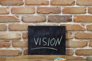 Chalk board with the word VISION drown by hand and chalks on wooden table on brick wall background. photo
