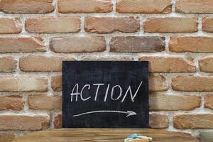 Chalk board with the word ACTION drown by hand and chalks on wooden table on brick wall background. photo