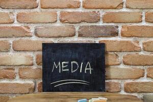 Chalk board with the word MEDIA drown by hand and chalks on wooden table on brick wall background. photo